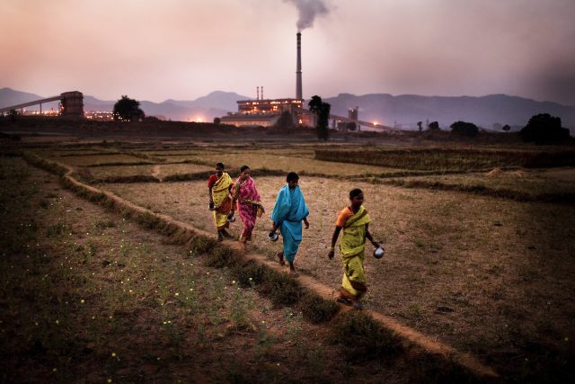 © Sanjit Das Women walk past a field against the background of Vedanta plant in Ijirupa village in Lanjigarh, Orissa, India. The huge bauxite deposits in Niyamgiri have led the Vedanta group to set up an alumina refinery at Lanjigarh, making the tribals apprehensive about their habitat. The UK based Vedanta Resources has come under immense pressure from human rights and environmental groups to abandon its plans to mine at the Niyamgiri mountains in Orissa for bauxite (to extract aluminium). The dig site is considered a sacred ground by the local Dongria Kondh community and has attracted support from conservationists from across the world.